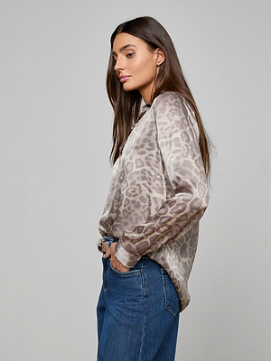 Woman with long brown hair wears the Tyler Silk Blouse, a gray leopard print button-down by L'AGENCE, paired with blue jeans and standing in profile against a plain light gray background.