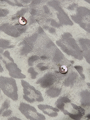 Close-up of the Tyler Silk Blouse in gray leopard print from L'AGENCE, showcasing two pearly buttons on the silky button-down fabric.
