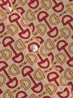 Close-up of the Holly Blouse by L'AGENCE, a beige slim-fit long sleeve button-down shirt featuring a horse bit print with red and yellow horseshoes linked by chains, finished with white buttons down the front.