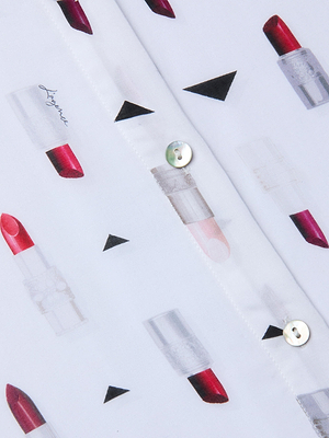 The Holly Blouse features white fabric with a lively pattern of red lipsticks and black triangles, accented by white buttons and a visible center seam, creating a playful slim fit lipstick print blouse.