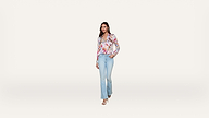A woman in a colorful blouse and light blue jeans stands against a plain white background, with one hand in her pocket and the other relaxed by her side.