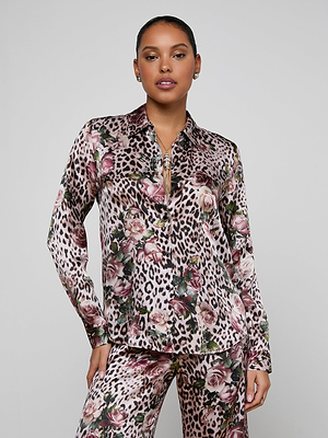 A woman poses confidently in the Tyler Silk Blouse and matching pants, showcasing a mixed rose cheetah print with floral accents in shades of pink, beige, and green. The silky outfit features a zippered neckline against a plain light gray background.