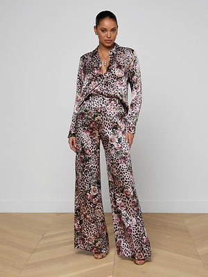 A woman stands confidently against a plain white wall, wearing the Tyler Silk Blouse and strappy heels.