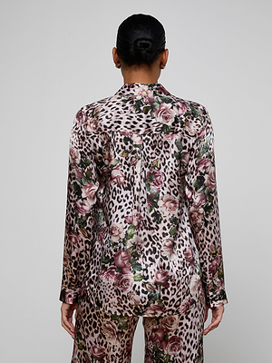 A person with dark hair in a low bun is shown from behind, wearing the Tyler Silk Blouse and matching pants set featuring rose cheetah print with floral and leopard patterns in pink, green, and beige.