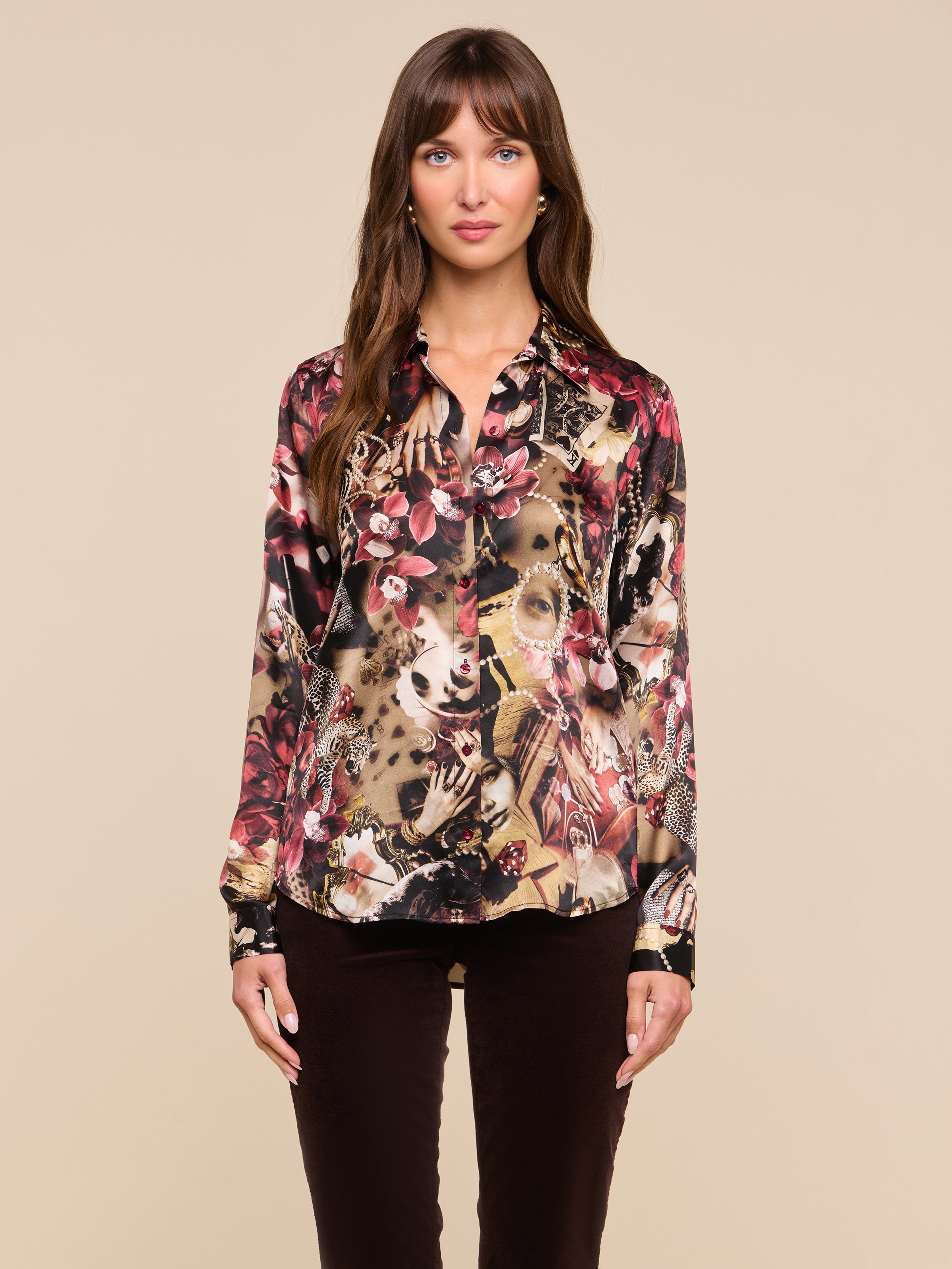 A woman stands against a plain background, wearing the Tyler Silk Blouse—a slim-fit, long-sleeve, floral-patterned top—paired with dark pants. She looks directly at the camera with her hands by her sides.