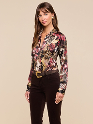A woman stands against a light background, wearing the slim-fit Tyler Silk Blouse with a statement print, tucked into dark pants with a belt. She looks at the camera with a slight smile.