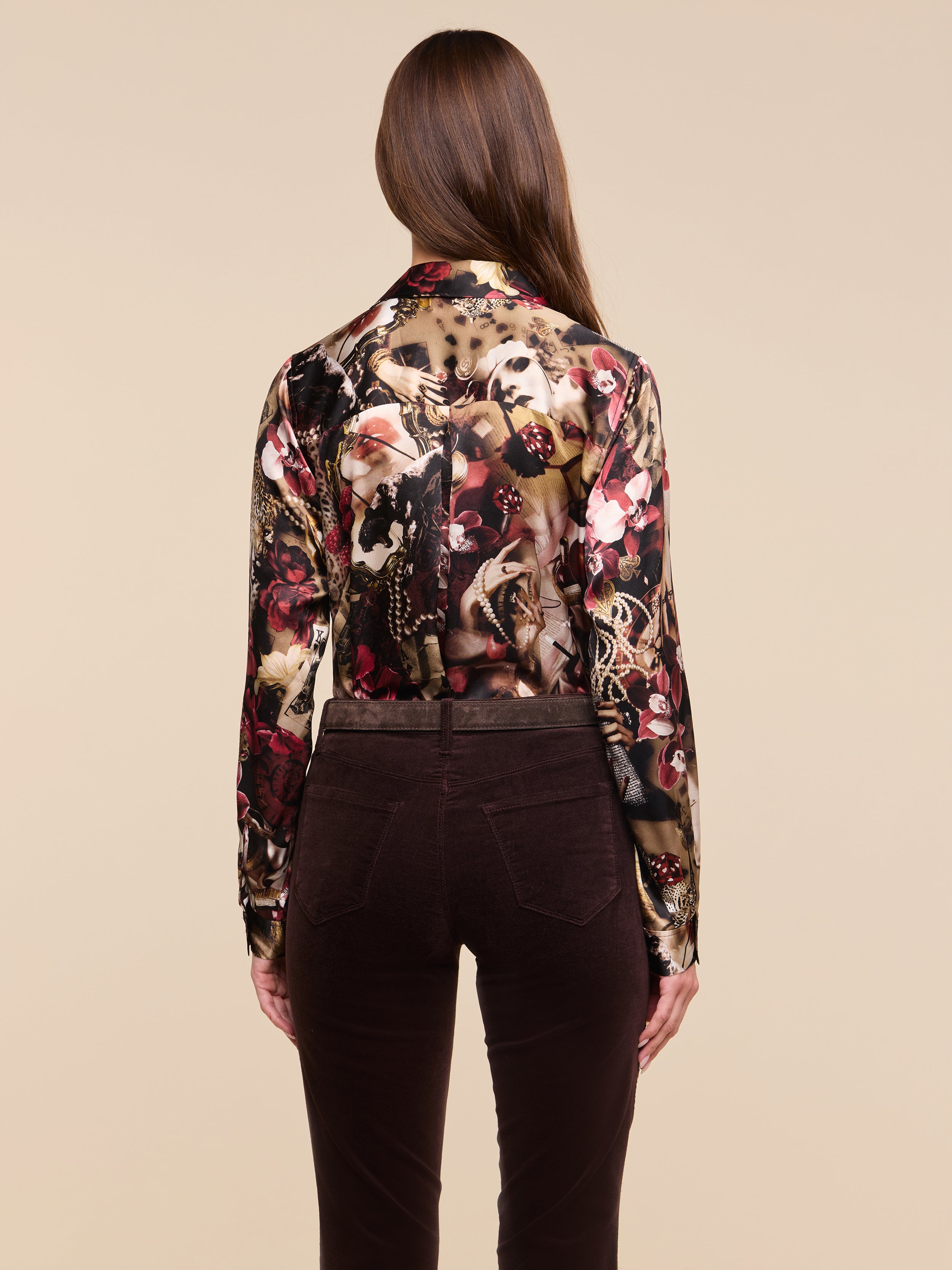 A woman with long brown hair, seen from behind, wears the Tyler Silk Blouse—a sheer, statement print long-sleeve top—paired with high-waisted dark brown pants against a plain light background.