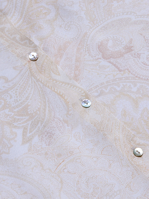 A close-up of the Tyler Silk Blouse highlights its long sleeves, pale paisley-print silk fabric, and three pearl-like buttons arranged diagonally.
