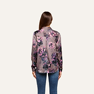 A woman with long brown hair, seen from the back, wears the Tyler Silk Blouse in a purple floral print paired with blue jeans, standing against a plain light background.