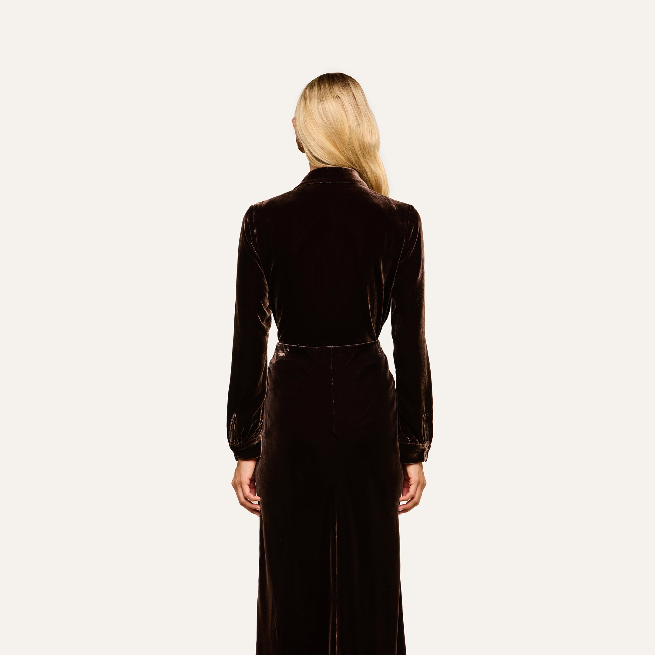 A woman with long blonde hair wears the Argo Velvet Blouse in dark java brown, featuring long sleeves, as she faces away from the camera against a plain, light background.