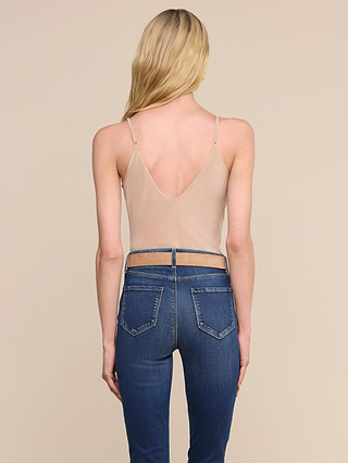 Una donna dai lunghi capelli biondi, vista di spalle, indossa la canotta Lexi Silk — un top color carne dal taglio sbieco con spalline regolabili — abbinata a jeans blu a vita alta su uno sfondo beige a tinta unita.