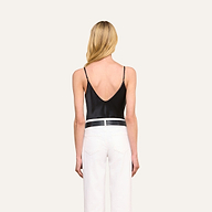 A woman with long blonde hair, dressed in the Lexi Silk Camisole with adjustable spaghetti straps and white pants, stands with her back to the camera against a plain light background.