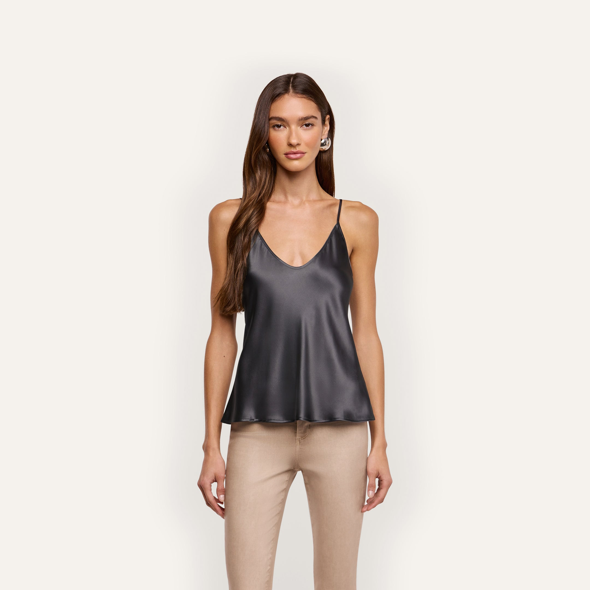 A woman wearing a black silk charmeuse Lexi Silk Camisole with a V-neck, thin straps, and tan pants.