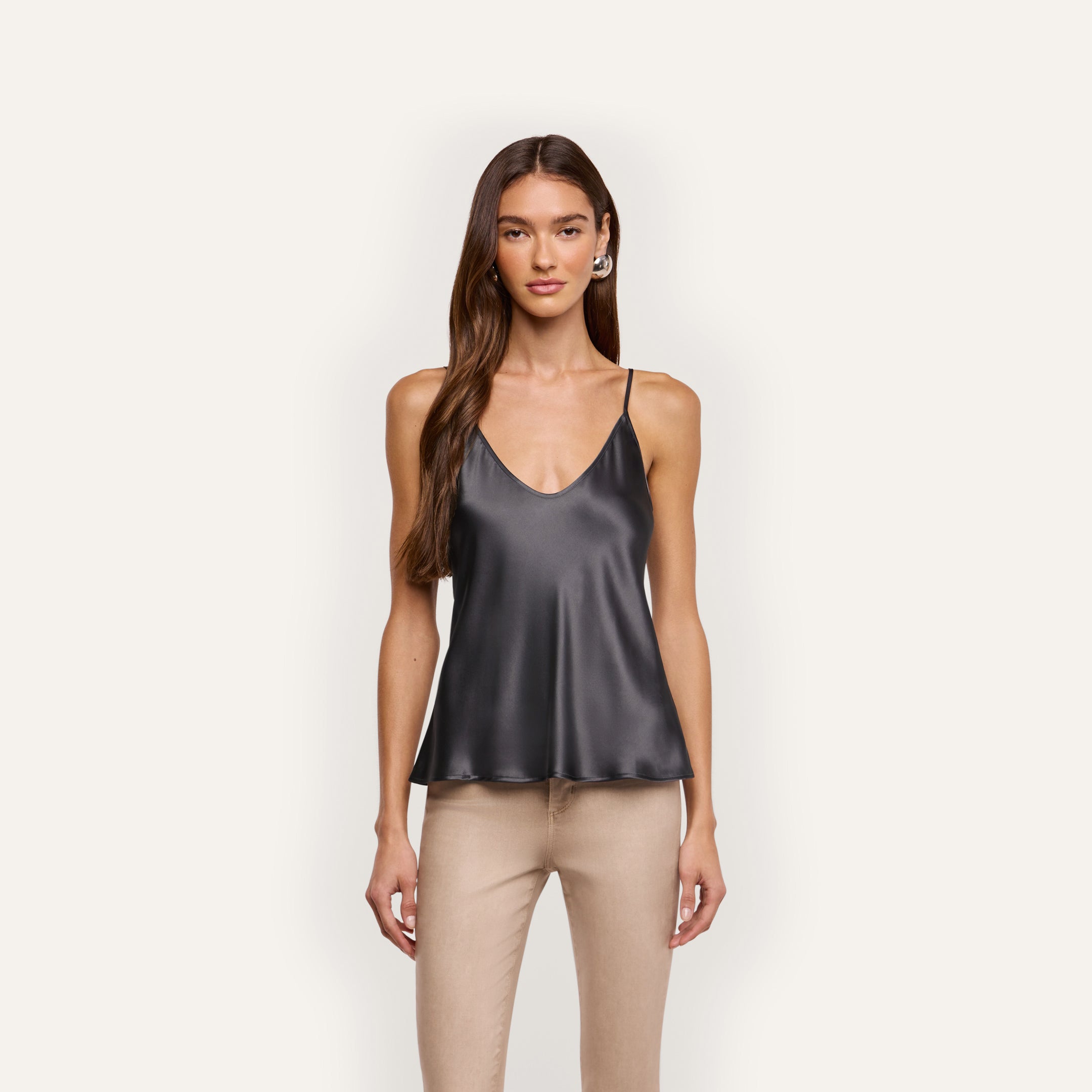 A woman wearing a black silk charmeuse Lexi Silk Camisole with a V-neck, thin straps, and tan pants.