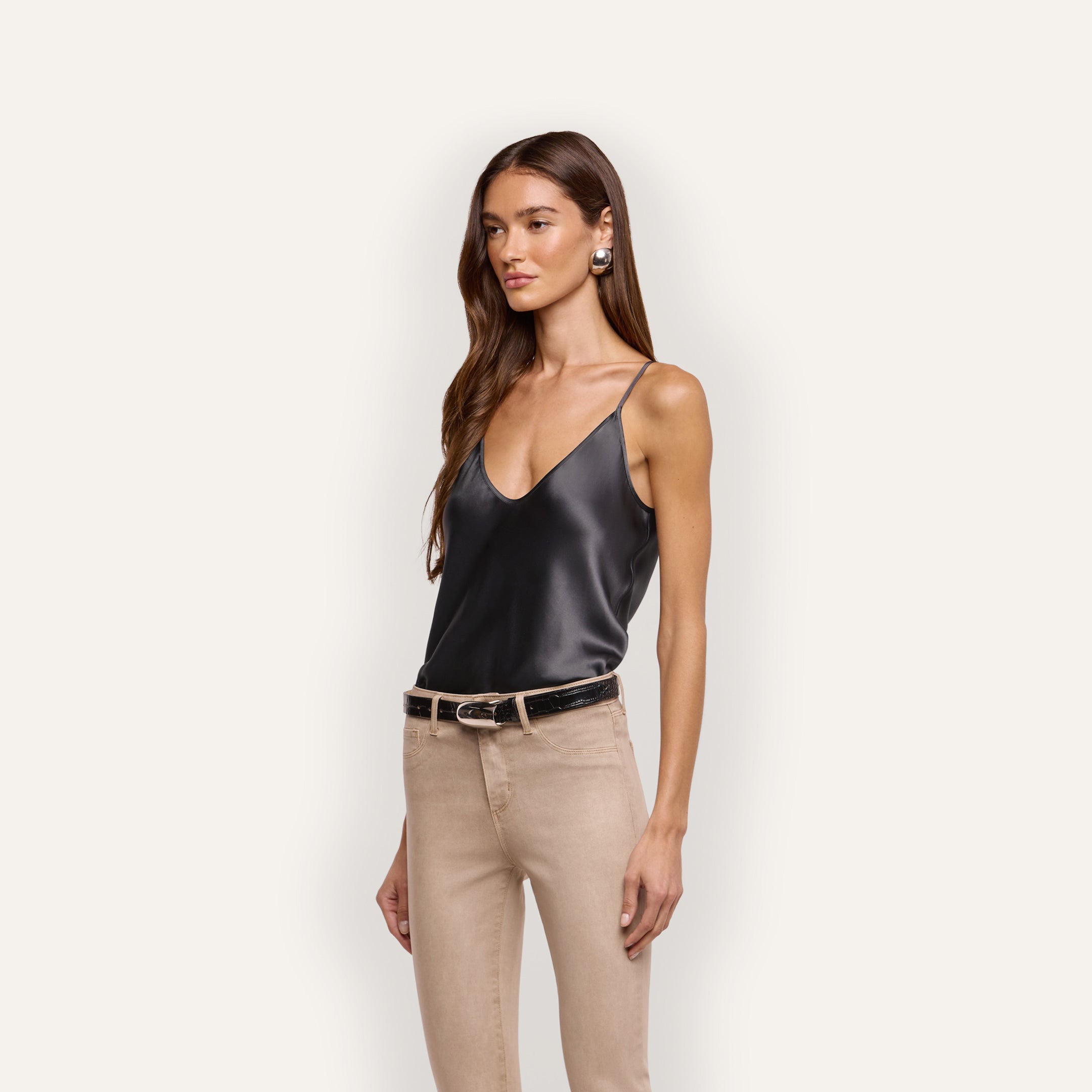 A woman wearing a bias-cut silk charmeuse V-neck Lexi Silk Camisole tucked into beige pants with a black belt.