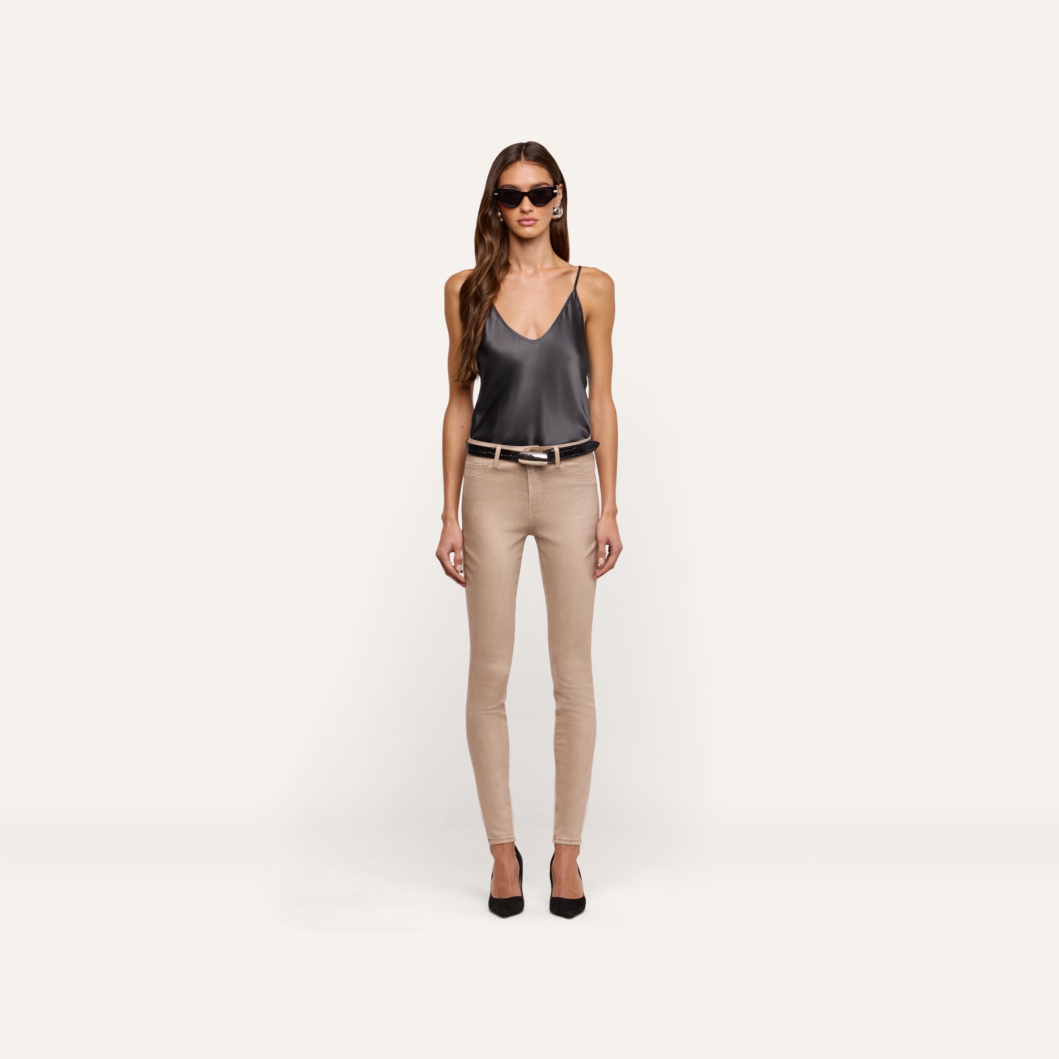 A woman wears a dark grey silk Lexi Silk Camisole, beige skinny jeans with a black belt, and black pointed-toe heels.