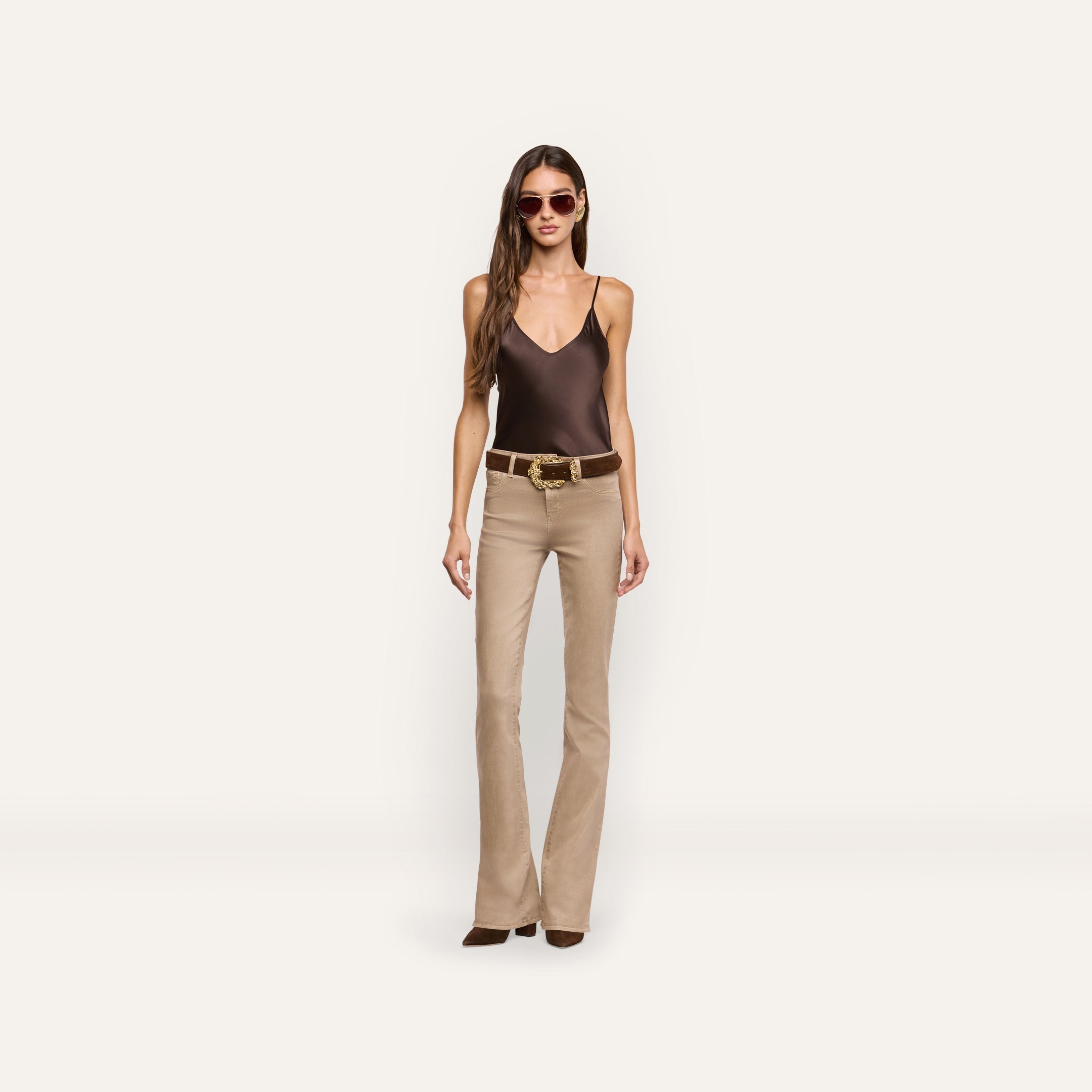 A person wearing a brown silk Lexi Silk Camisole, a brown belt with a decorative gold buckle, and tan flared pants.