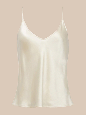 The Lexi Silk Camisole, in a cream hue, features bias-cut silk charmeuse, thin spaghetti straps, and a V-neckline. It is shown against a neutral beige background.