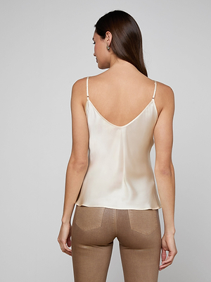 A woman with long brown hair models the Lexi Silk Camisole in cream, featuring adjustable straps, paired with light brown pants as she stands with her back to the camera against a plain gray background.