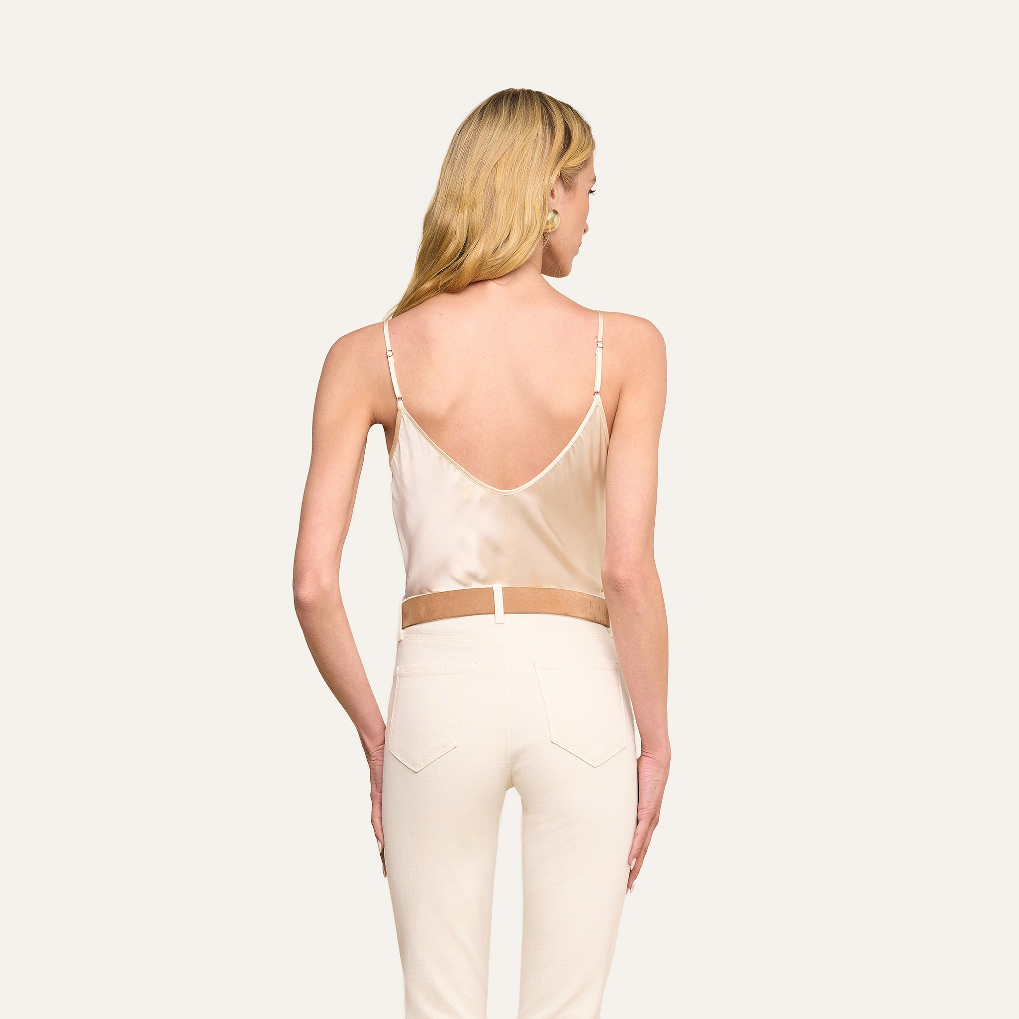 Woman with long blonde hair shown from the back, wearing the Lexi Silk Camisole in pearl white with thin straps and off-white pants, standing against a plain light background.