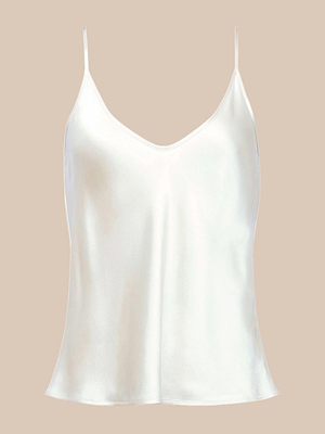 The Lexi Silk Camisole is a silky white charmeuse top with thin adjustable straps, a V-neckline, and a loose, slightly flared fit, shown against a beige background.