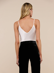 A person with long blonde hair, dressed in the Lexi Silk Camisole with adjustable straps and black pants, is standing and facing away from the camera against a plain light background.