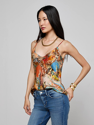 A woman with long black hair models the Lexi Satin Camisole with adjustable straps, paired with blue jeans, gold chain necklace, and gold bangles, posing with one hand on her hip against a plain gray background.
