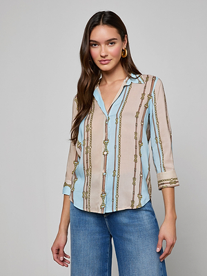 A woman with long brown hair wears the Camille Blouse, featuring three-quarter sleeves and a blue and beige striped belt print with gold accents, paired with blue jeans against a plain light gray background.