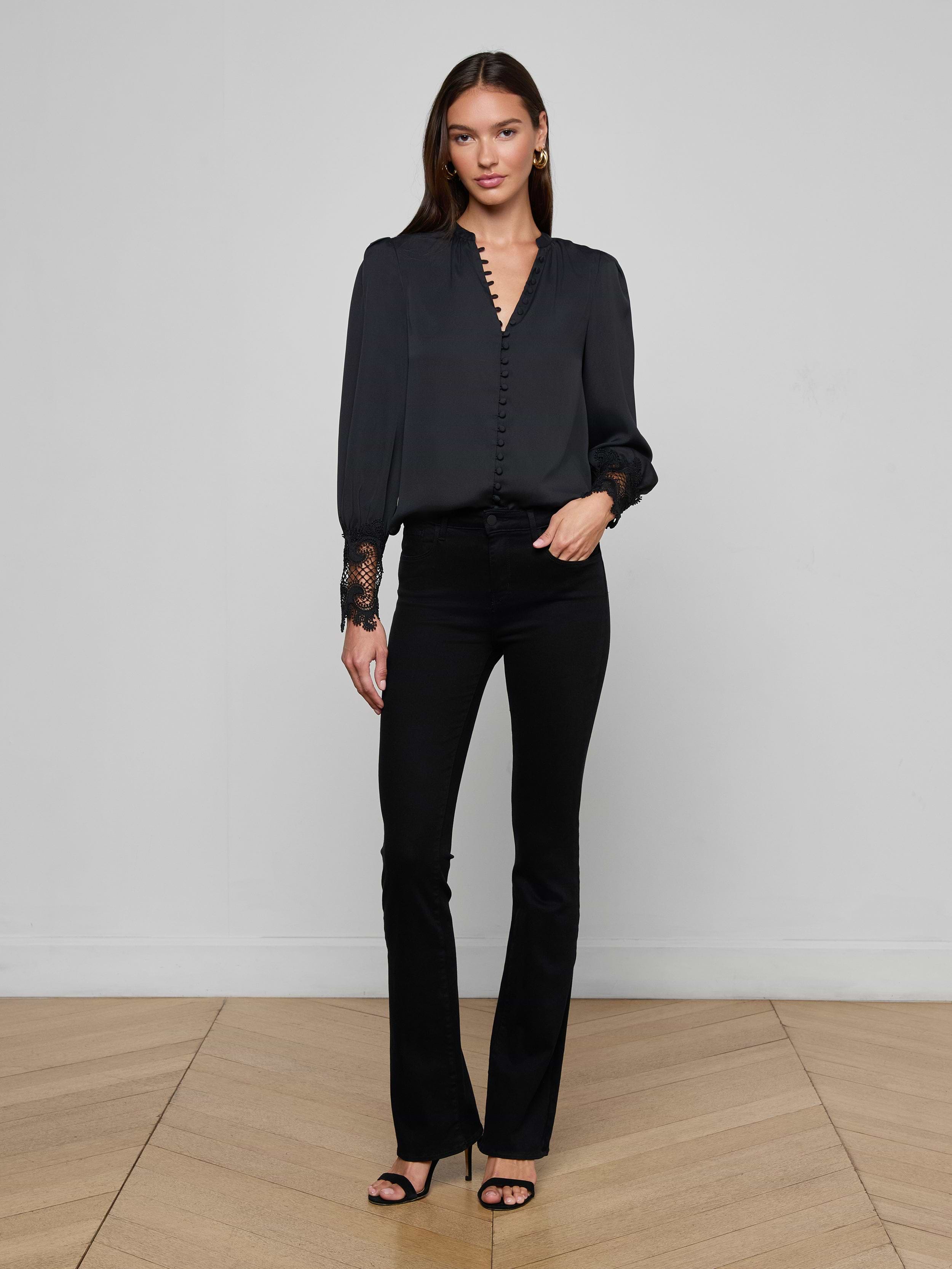 A woman stands against a plain white background wearing the Ava Blouse, styled with blue high-waisted jeans, a black belt featuring a gold buckle, and black heels.