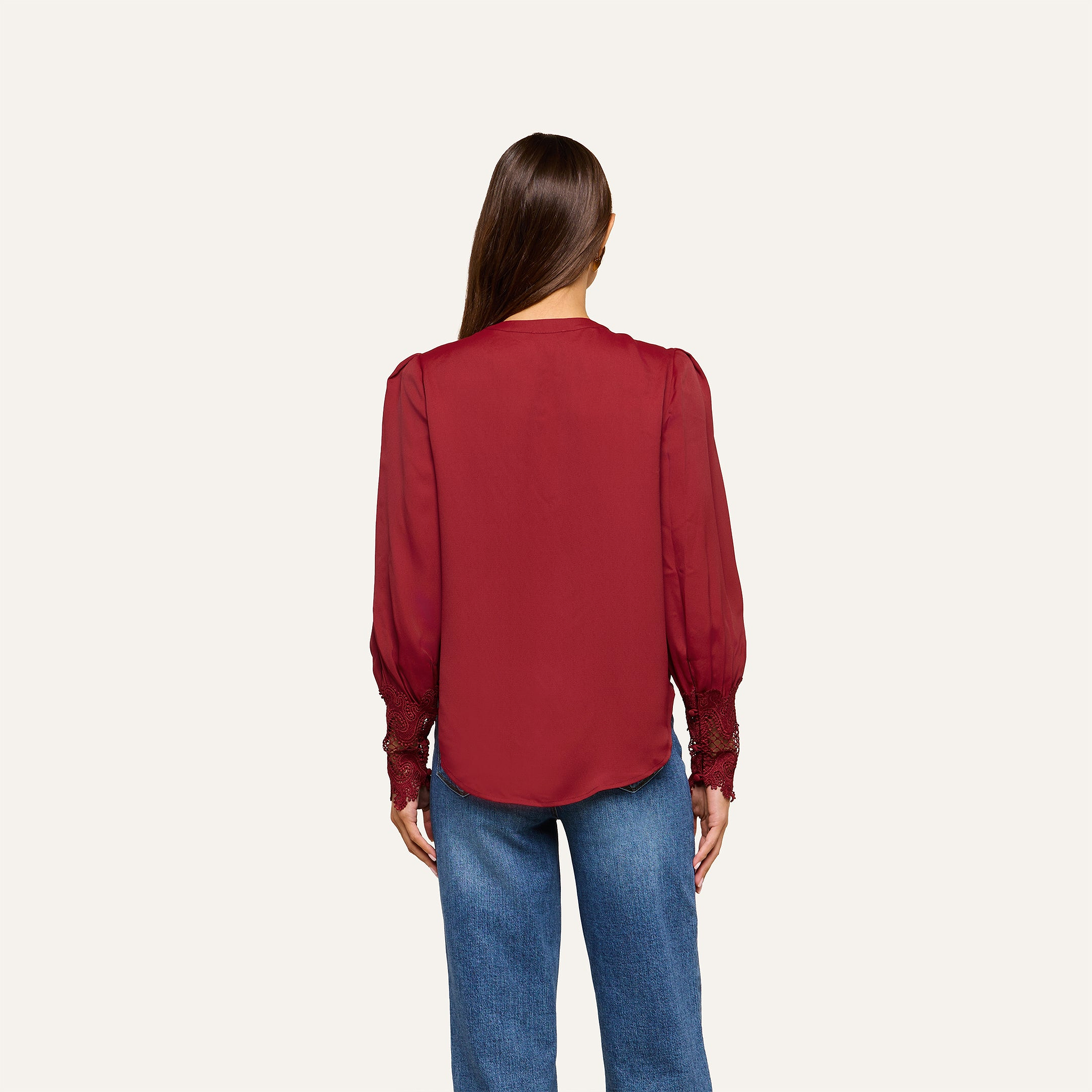 A woman with straight brown hair is seen from behind, wearing the Ava Blouse—a vintage-inspired top with puff sleeves—paired with blue jeans against a plain light background.
