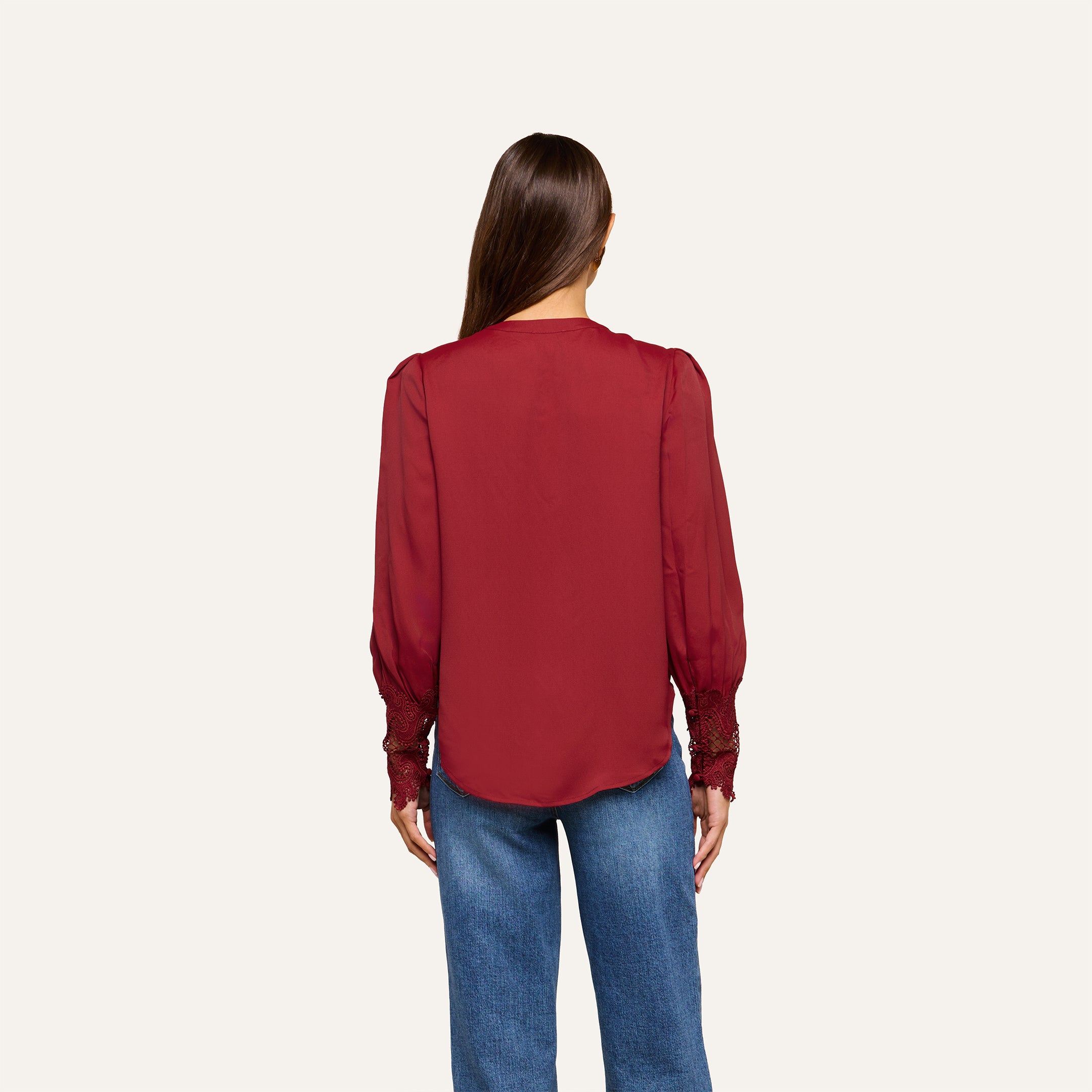 A woman with straight brown hair is seen from behind, wearing the Ava Blouse—a vintage-inspired top with puff sleeves—paired with blue jeans against a plain light background.