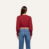 A woman with long brown hair, seen from behind, wears the Ava Blouse—featuring vintage-inspired scalloped lace detailing—paired with blue jeans, standing against a plain light background.