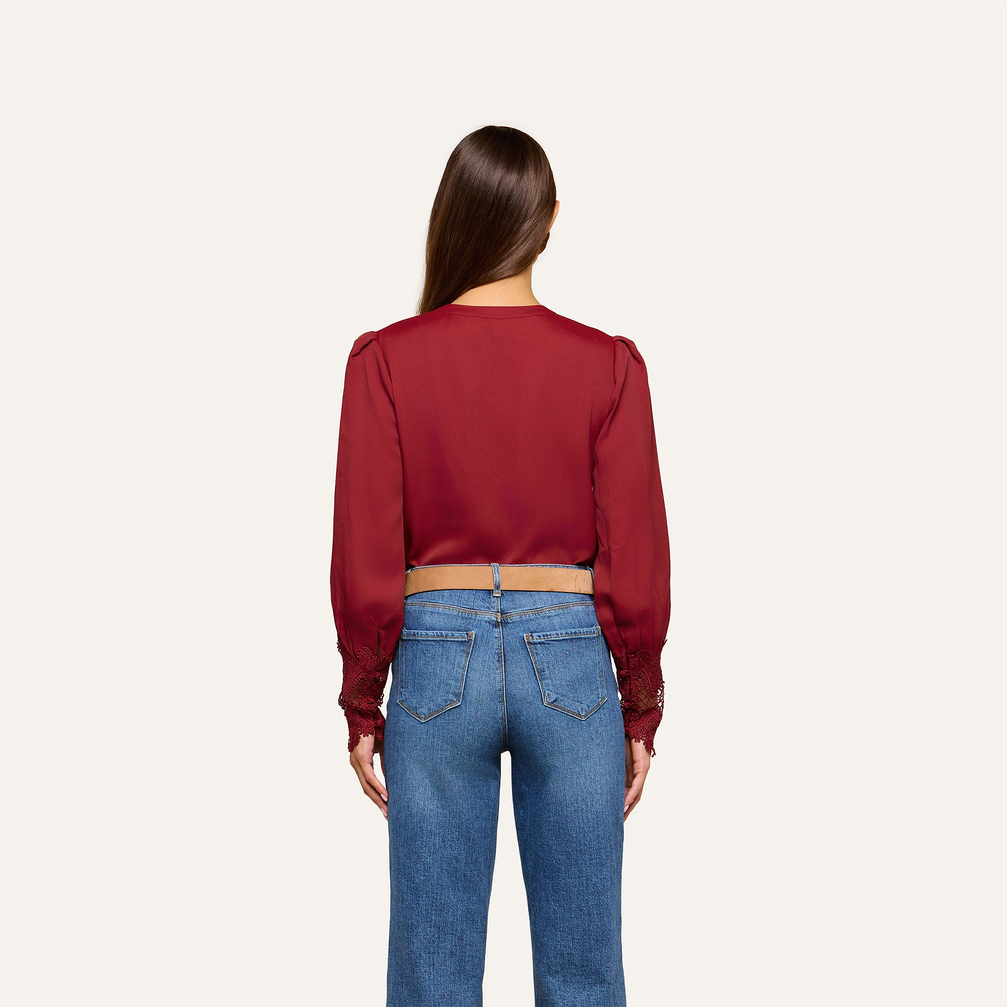 A woman with long brown hair, seen from behind, wears the Ava Blouse—featuring vintage-inspired scalloped lace detailing—paired with blue jeans, standing against a plain light background.