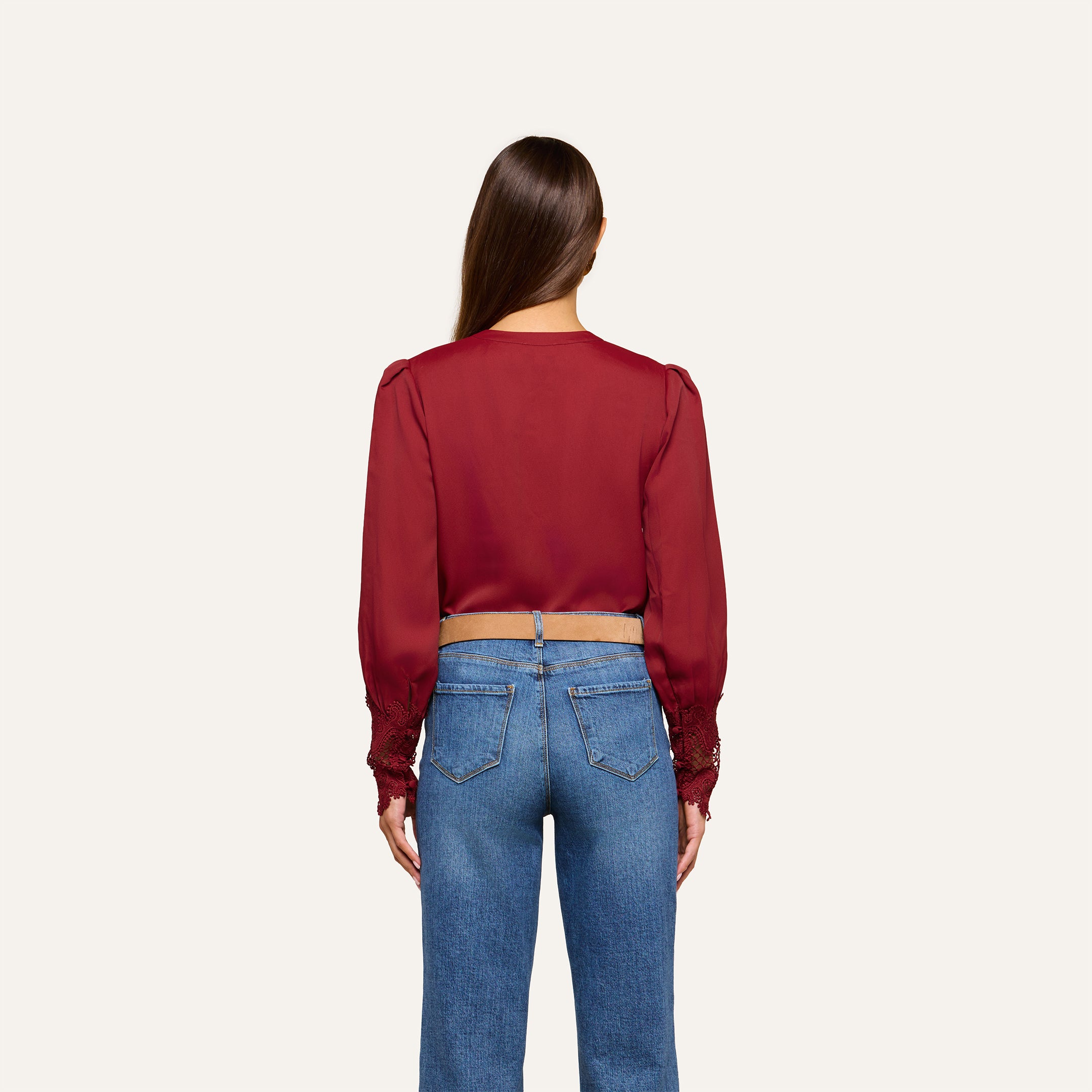 A woman with long brown hair, seen from behind, wears the Ava Blouse—featuring vintage-inspired scalloped lace detailing—paired with blue jeans, standing against a plain light background.