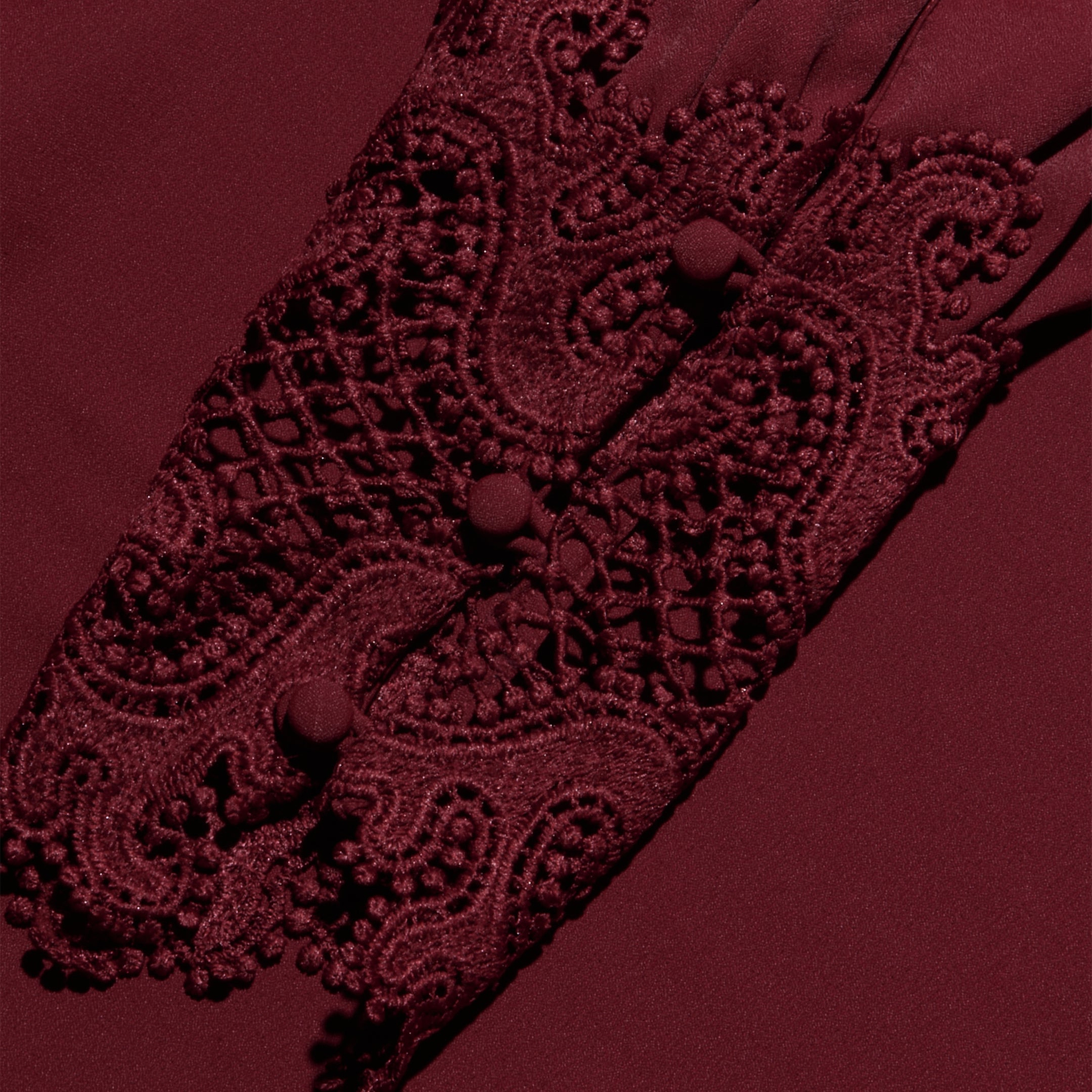 The Ava Blouse showcases detailed burgundy lace sleeves adorned with decorative buttons and an intricate embroidered pattern, featuring scalloped lace accents for a vintage-inspired effect, all set against a coordinating burgundy fabric background.