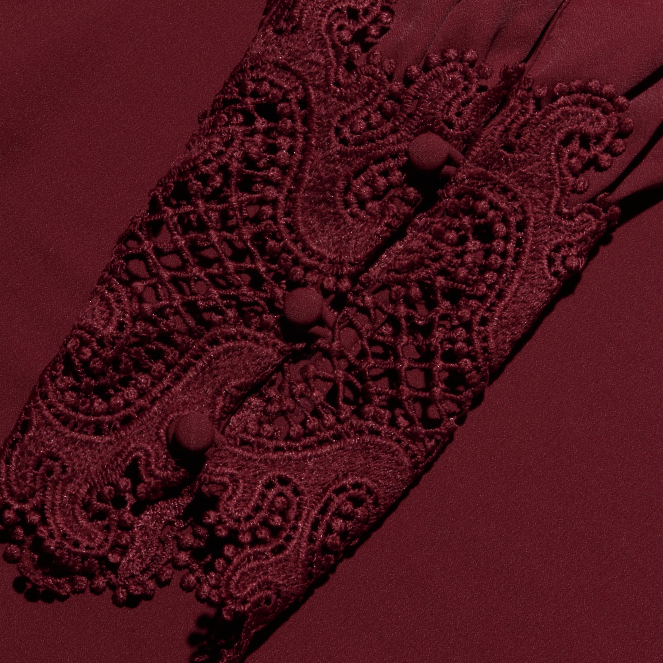 The Ava Blouse showcases detailed burgundy lace sleeves adorned with decorative buttons and an intricate embroidered pattern, featuring scalloped lace accents for a vintage-inspired effect, all set against a coordinating burgundy fabric background.