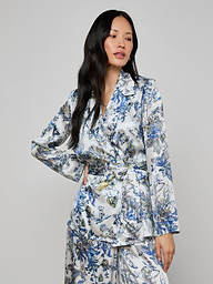 A woman with long black hair wears the Ciara Silk Robe Top in a blue, green, and white floral pattern, standing against a plain light gray background.