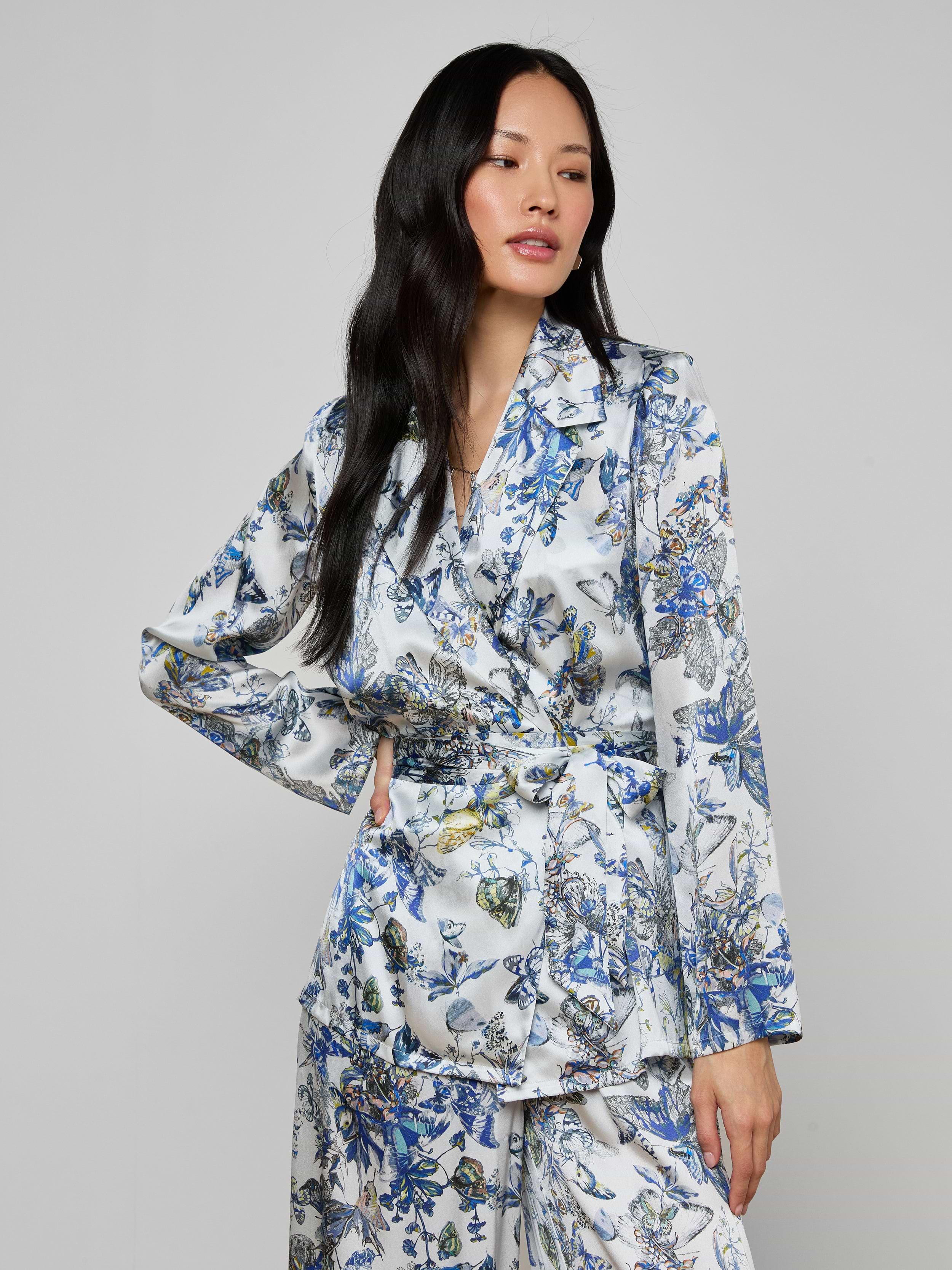 A woman with long black hair wears the Ciara Silk Robe Top in a blue, green, and white floral pattern, standing against a plain light gray background.
