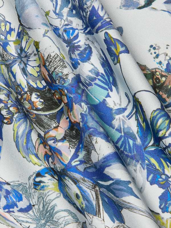 The Ciara Silk Robe Top features silk charmeuse in a watercolor-style floral and leaf pattern of blue, teal, yellow, and orange on white. Softly draped, its perfect for an elegant evening jacket look.