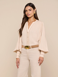 A woman wears the Kiera Blouse—a beige, textured rayon bohemian top with blouson sleeves—paired with beige pants, a brown belt, gold earrings, and her long dark hair styled loosely against a plain white background.