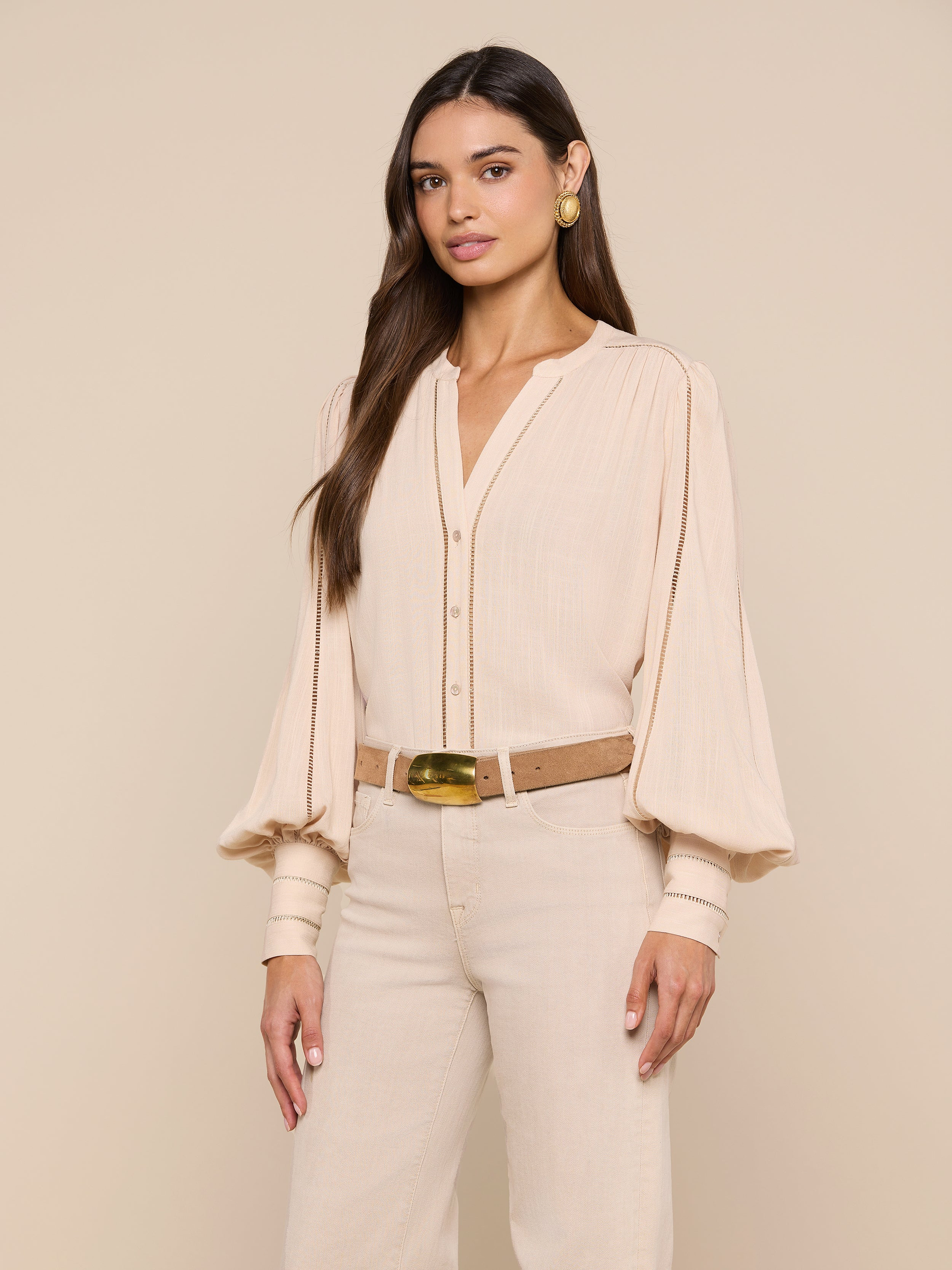 A woman wears the Kiera Blouse—a beige, textured rayon bohemian top with blouson sleeves—paired with beige pants, a brown belt, gold earrings, and her long dark hair styled loosely against a plain white background.