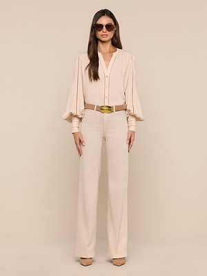 A woman in the Kiera Blouse with blouson sleeves, wide-leg beige pants, a tan belt, and platform shoes poses against a beige background. She has long dark hair and sunglasses.