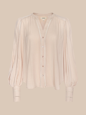The Kiera Blouse is a light pink, long-sleeve bohemian top featuring a loose fit, button-down front, gathered shoulders, cuffed blouson sleeves, and lace trim on the placket and cuffs. Made from lightweight textured rayon.