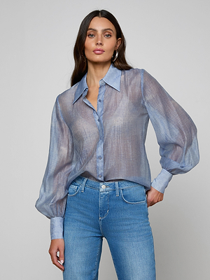 A woman with long brown hair wears the Jayleen Blouse, a sheer chiffon button-down with blouson sleeves, paired with light blue jeans against a plain gray background.