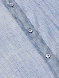 Close-up of the Jayleen Blouse: a light blue, textured button-down shirt featuring a subtle, irregular pattern and a row of white buttons with visible stitching along the vertical seam.