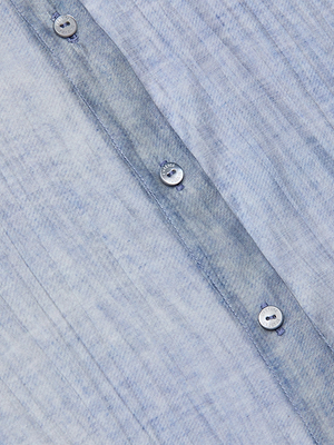 Close-up of the Jayleen Blouse: a light blue, textured button-down shirt featuring a subtle, irregular pattern and a row of white buttons with visible stitching along the vertical seam.