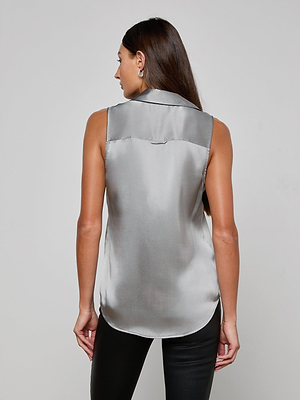 A woman with long brown hair is seen from behind, wearing the Emmy Sleeveless Silk Blouse in silver charmeuse and black pants against a light-gray background—ideal for transitioning from office to evening.