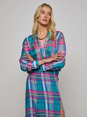 A woman with long blonde hair stands with arms crossed, wearing the Cosette Plaid Shirt and a matching skirt in blue, pink, and teal hues, accessorized with layered necklaces and hoop earrings against a neutral background.