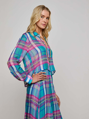 A woman with long blonde hair poses against a plain light background, wearing the Cosette Plaid Shirt—a vibrant cropped button-down dress in blue, pink, and purple plaid, with one hand on her hip.