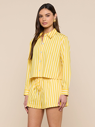 A woman wearing the Cosette Shirt—yellow and white vertically striped and tailored—with matching striped drawstring shorts, standing against a plain light background.